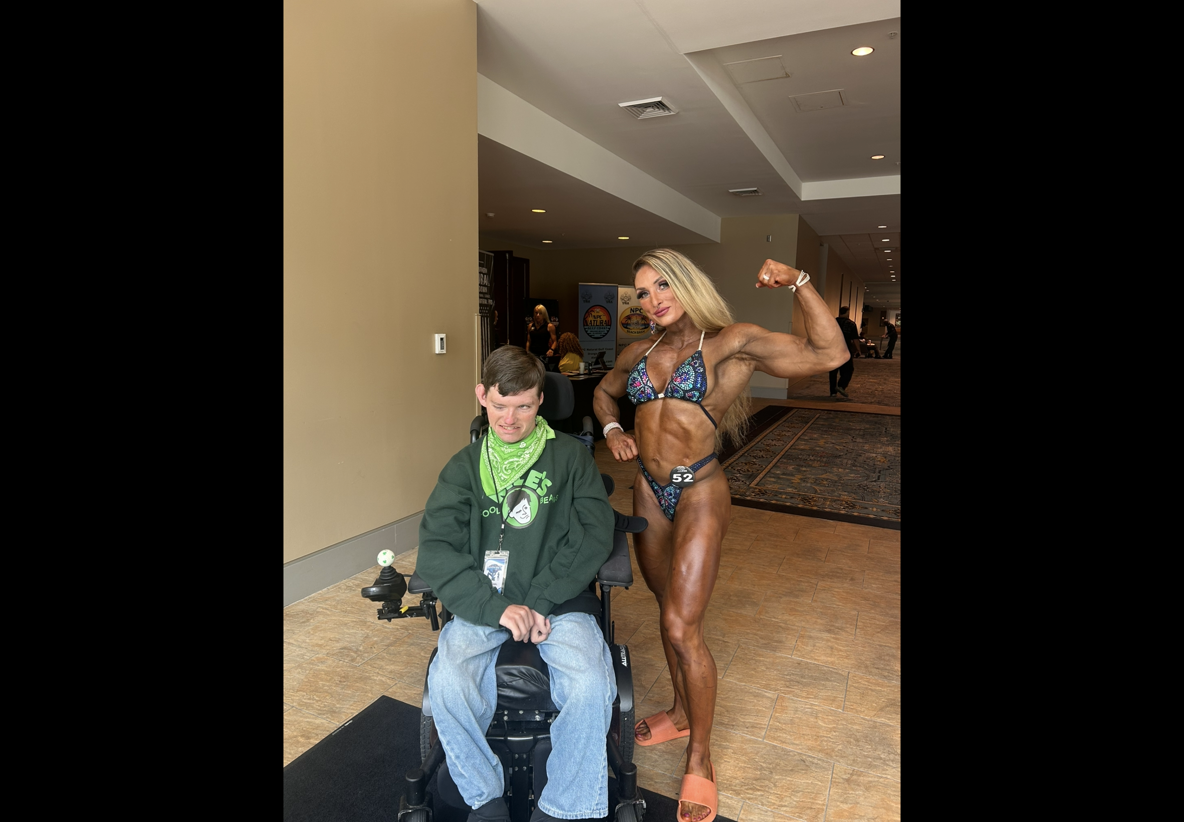 Woman in a fitness competition posing next to Kyle in a wheelchair.