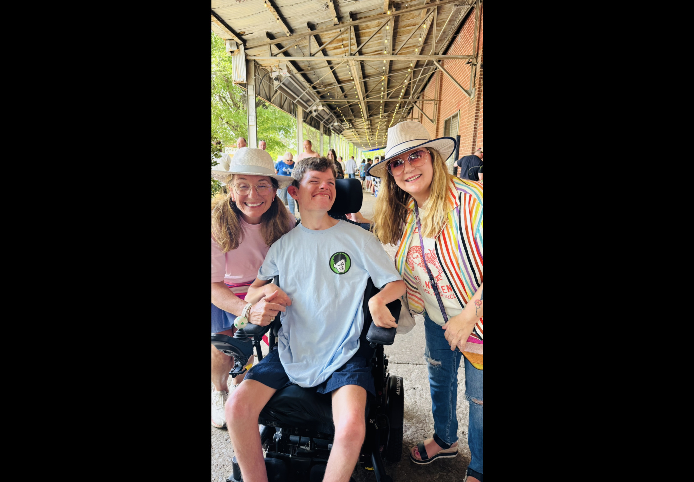 Person in a wheelchair with two friends outdoors, wearing hats.